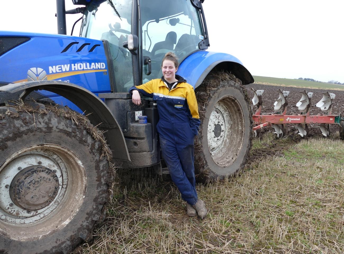An agriculture apprentice leans against a tractor
