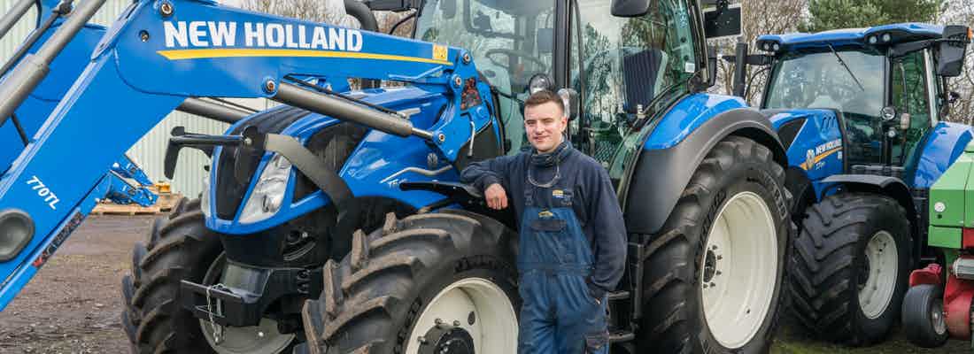 Land-based engineer standing beside New Holland blue tractor