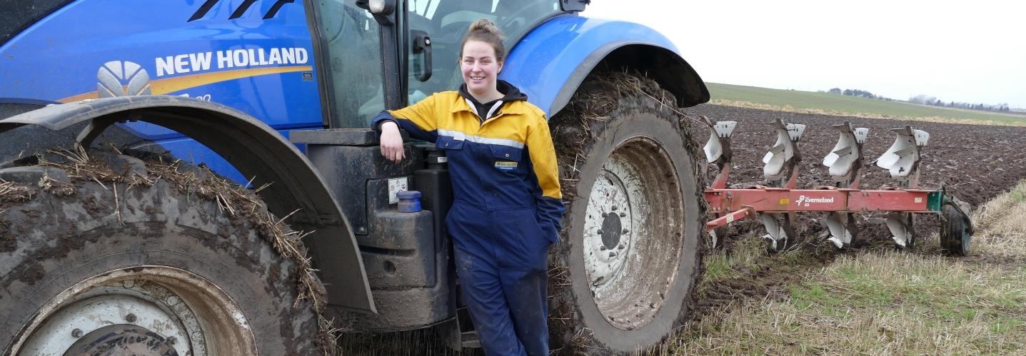 An agriculture apprentice leans against a tractor