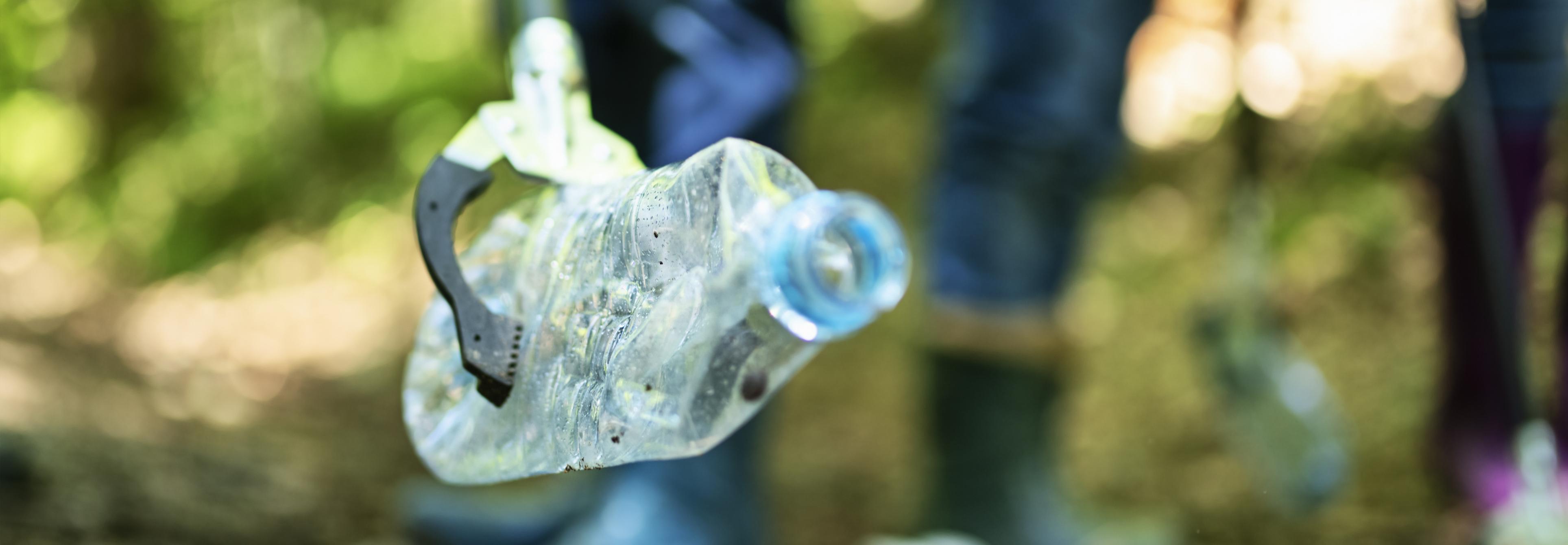 Plastic litter being picked up in a forest by a grab with people standing behind 