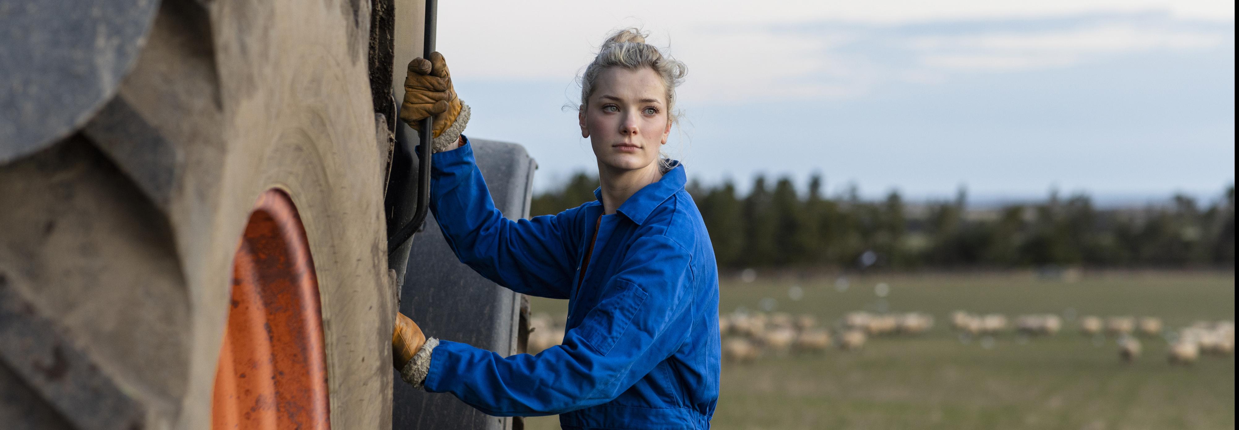 Woman in blue boiler suit standing beside a tractor