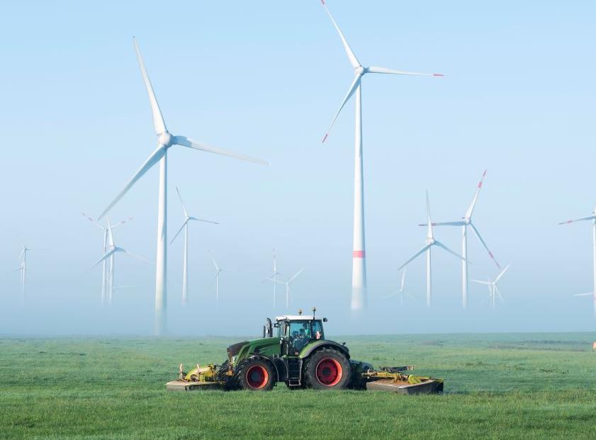 Tractor cutting grass in front of wind farm