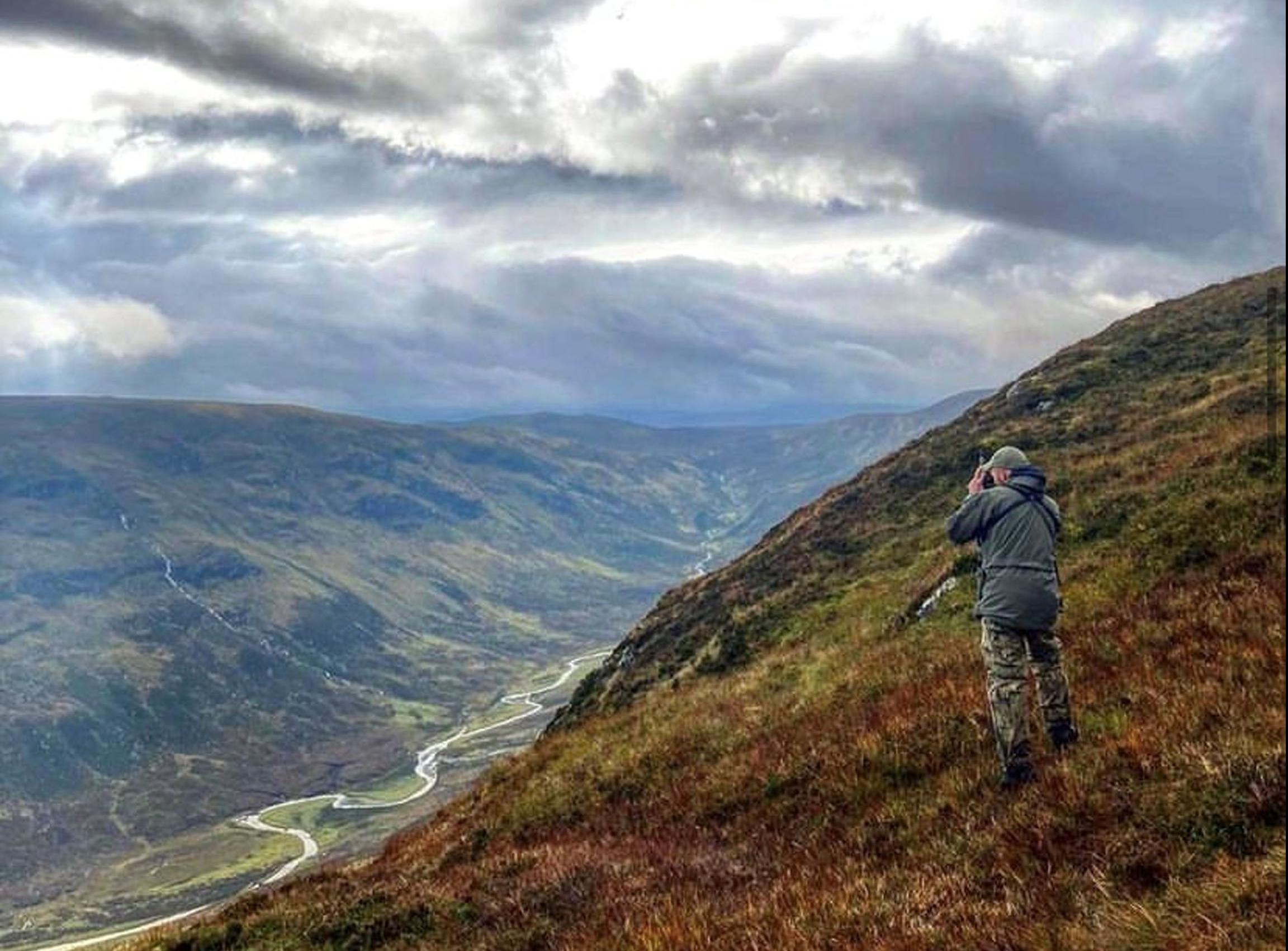 Gamekeeper using binoculars on a hill above a valley in Scotland