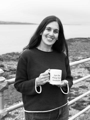 Jill Couto-Phoenix of Lantra holding a mug in front of a shoreline
