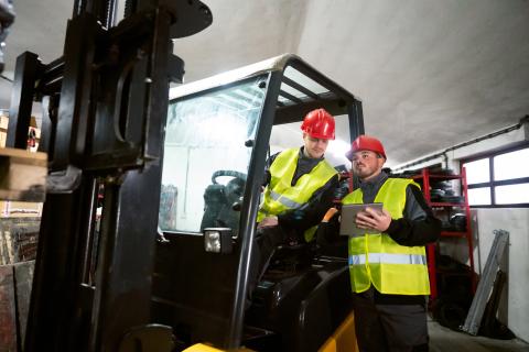 Two workers with safety gear on meeting beside a forklift